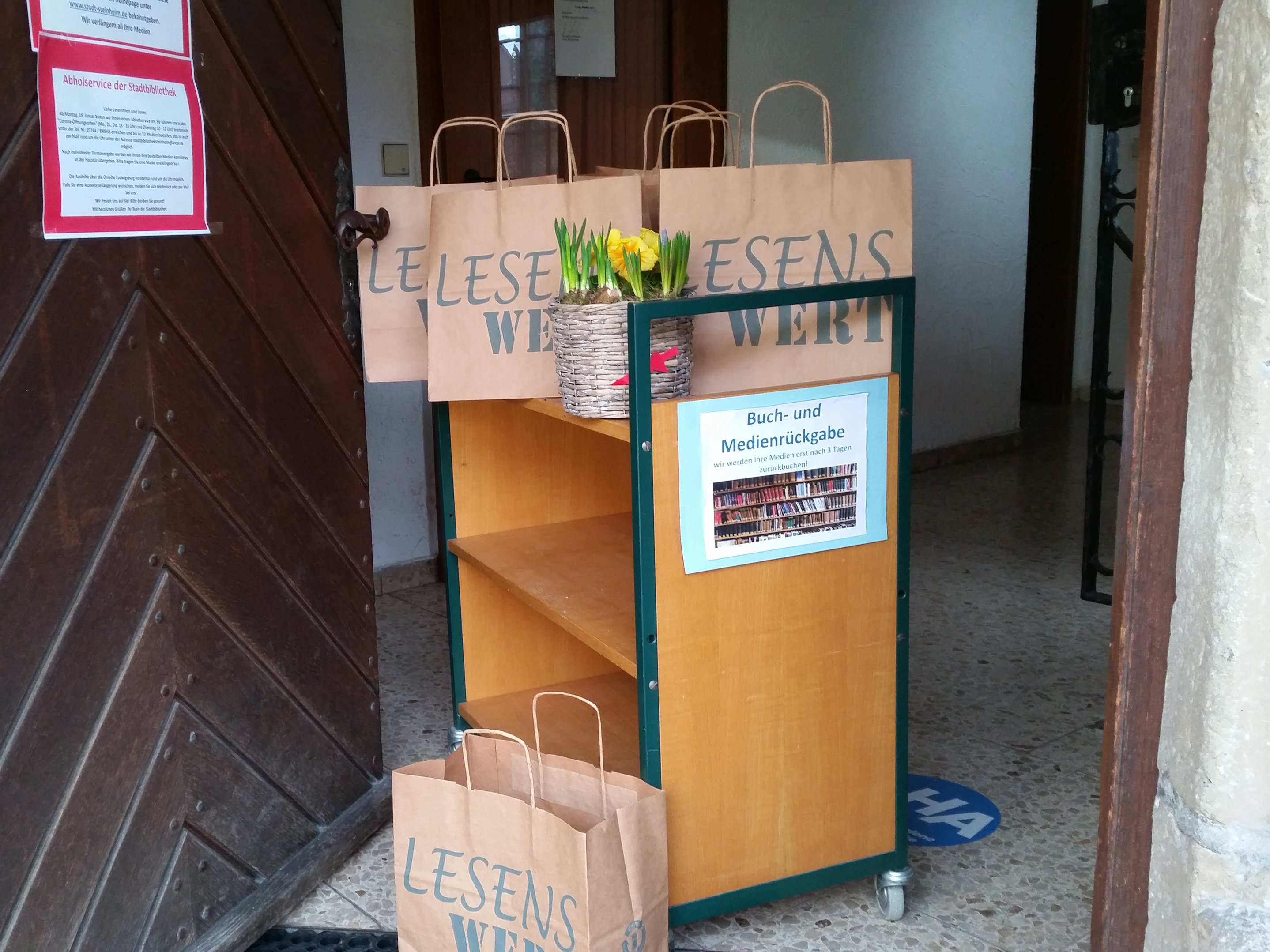 Abholservice bei der Stadtbibliothek Eingangsbereich - offene Tür mit Regal und Papiertüten